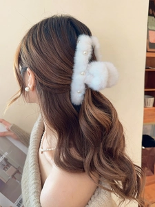 Close-up of large white plush hair claw clip with pearl accents worn by a model