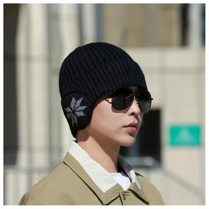 Detail of black winter knit hat with ear flaps and grey snowflake patterns outdoors