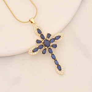 Macro detail of 18K gold cross pendant with blue marquise stones and snake chain