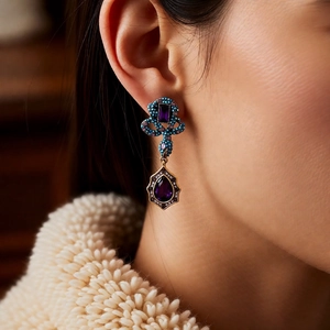 Close-up of vintage drop earrings with purple crystals and turquoise-toned pavé stones