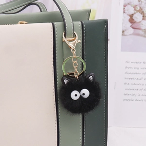 Close-up of a black fluffy coal ball bag charm with white eyes and golden metal clasp