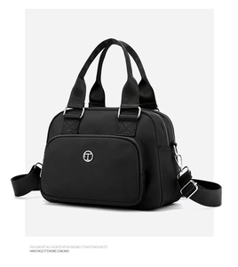 Detail of black nylon tote bag with silver circular metal logo and reinforced handle strap