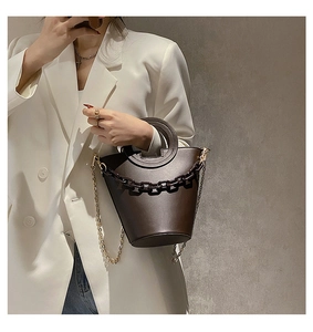 Detail of dark brown bucket bag with hollow round handle and chunky chain on white blazer
