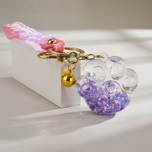Detail of purple acrylic cat paw keychain with liquid glitter and golden bell