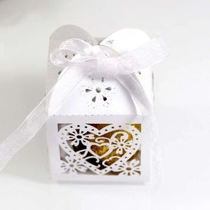 Close-up of white laser-cut heart favor box with elegant satin ribbon and gold detail