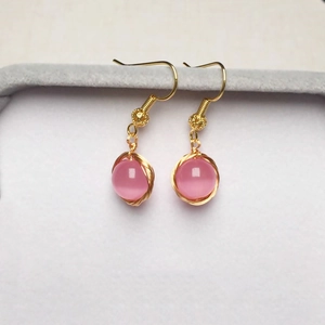 Gros plan détaillé de boucles d'oreilles or 14K avec perles œil de chat rose sur velours