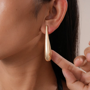 Close-up of long gold teardrop earring worn by model to show glossy finish and texture