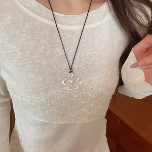 Detail of silver hollow flower pendant on a black cord necklace worn on a white shirt