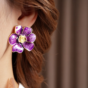 Detalle de pendiente de flor de esmalte morado con borde dorado usado por modelo