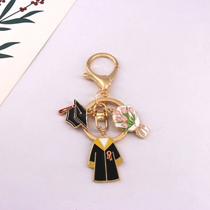 Detail of graduation keychain with black mortarboard and pink bouquet charms on purple background