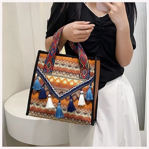 Detail of bohemian woven tote bag featuring vibrant geometric embroidery and blue tassels