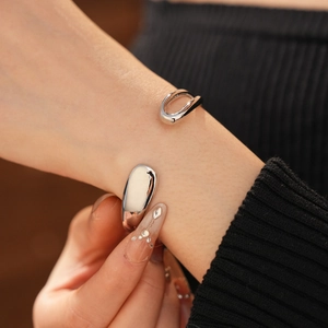 Close-up of minimalist silver open bangle featuring teardrop hollow geometric design