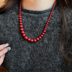 Gros plan d'un collier de perles rouges élégant sur un mannequin en pull gris foncé