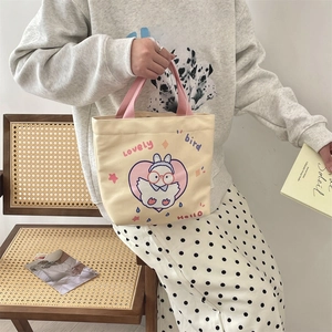 Detail of canvas tote bag with cute cartoon bird print and pink handles held by model
