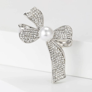 Silver bow brooch with pearls and sparkling rhinestones on a white geometric surface