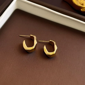 Detailed view of golden geometric C-shaped earrings with polished faceted metal surfaces