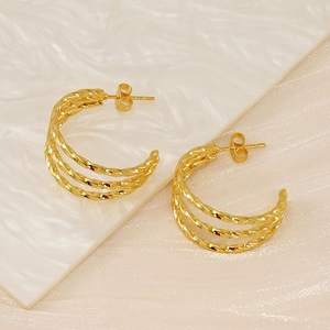 Detailed view of triple twisted gold hoop earrings on a textured minimalist background