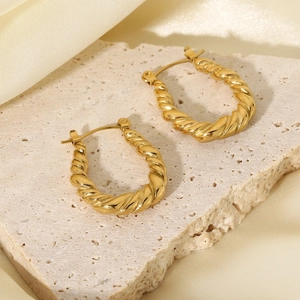 Close-up of gold plated stainless steel twisted hoop earrings on light stone