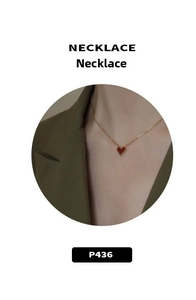 Close-up of a gold chain necklace with a red heart pendant worn with a dark green outfit