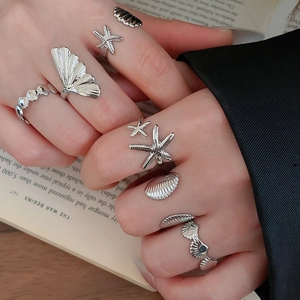 Close-up of silver starfish and seashell rings set worn on hand over a book