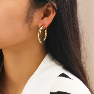 Detailed view of large gold hoop earring with elegant quilted pattern on model