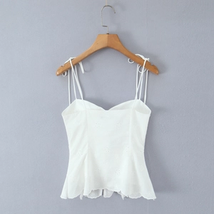 Detail view of a white lace embroidered camisole top with thin straps on a wooden hanger