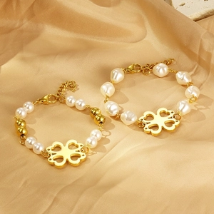 Detail of gold clover charm bracelets with white baroque pearls on warm silk background