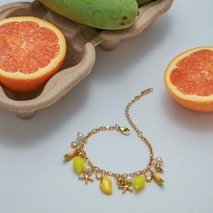 Detail of gold stainless steel bracelet with mango, lemon, and starfish charms