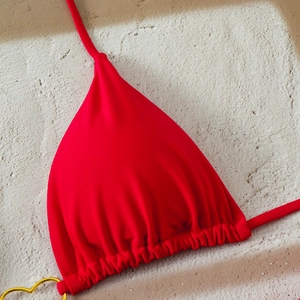 Detailed close-up of red bikini top with golden heart metal ring and pleated fabric