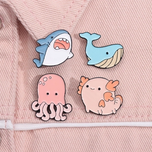 Detail of four cute marine animal enamel pins including shark and whale on pink denim