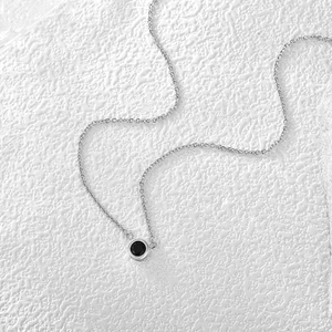 Detailed close-up of a silver-tone necklace with a round black zircon pendant on white texture