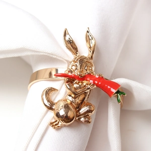 Macro shot of golden rabbit napkin ring with a red carrot detail on white linen fabric
