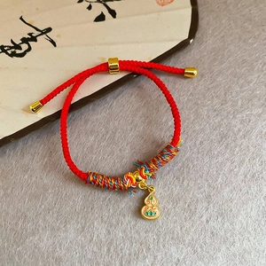 Gros plan du bracelet en corde rouge tressée avec breloque gourde dorée sur éventail blanc