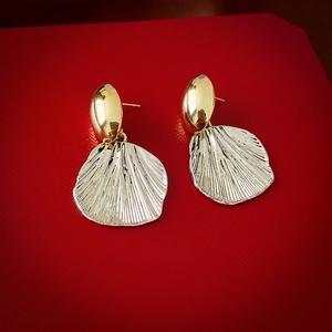 Detailed view of golden fan-shaped shell earrings on a luxury red leather background
