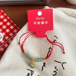 Detail of red braided bracelet featuring green beads and a golden mythical beast charm