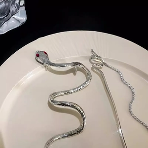 Detail of silver snake hair pin with red gemstone eyes resting on white ceramic tray