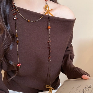 Detail of beaded necklace featuring red mushroom charm and yellow bow on model clothing