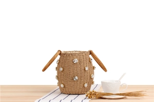 Detail of woven straw bucket bag with crystal embellishments on a wooden table