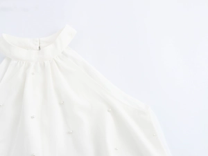 Detail eines weißen Halterneck-Kleides mit feinen Falten und Perlenverzierungen