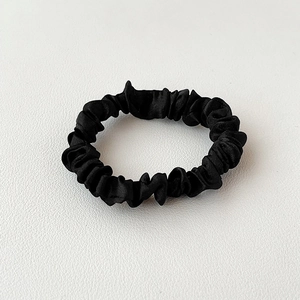 Detail of premium black satin scrunchie showing glossy silk texture on white leather