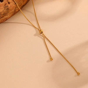 Detail of adjustable 18k gold snake chain necklace with sliding bead and tassels on wood