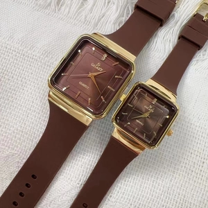 Orologi quadrati dorati con cinturini in silicone marrone su tessuto bianco