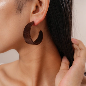 Close-up of a model wearing dark brown flocked C-shaped earrings with a velvet texture