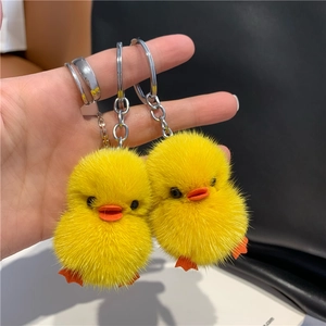 Close-up of two mini yellow plush duck keychains with silver metal rings and soft fur texture