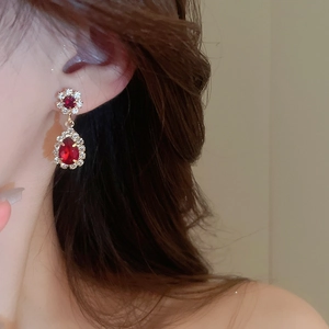 Close-up of elegant flower-shaped earrings with red crystal teardrops worn by a model
