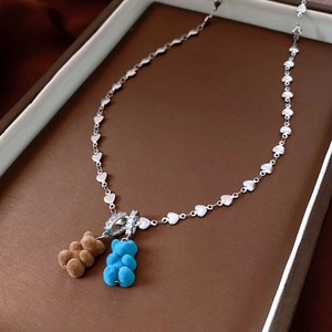 Détail de pendentifs ours marron et bleu sur une chaîne à maillons de cœur argentée