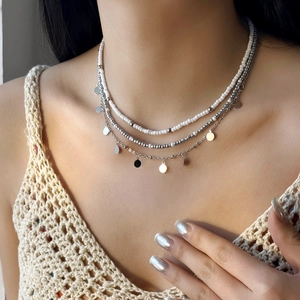 Gros plan du collier triple rang avec perles blanches et pendentifs argentés sur modèle