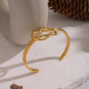 Detailed close-up of a minimalist gold knotted cuff bracelet on a white textured stone surface