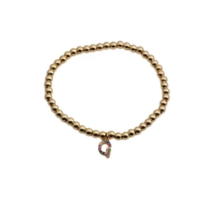 Macro shot of a golden bead bracelet with a Q-shaped pendant and colorful zircon stones