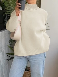 Dettaglio del maglione a collo alto color crema abbinato a jeans in denim azzurro